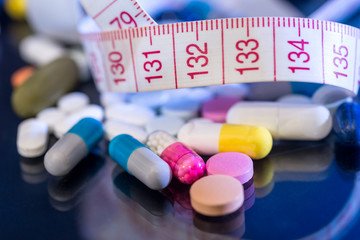 medical pills, vitamin tablets with measuring tape isolated on black background.