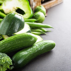 Mini cucumbers with assorted green vegetables, salad, broccoli, peas and Brussels sprouts on brown stone table top. Healthy food concept with copy space.