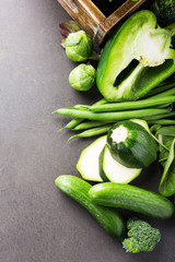 Background with assorted green vegetables, salad, broccoli, mini cucumber, peas and Brussels sprouts on brown stone table top. Healthy food concept with copy space.