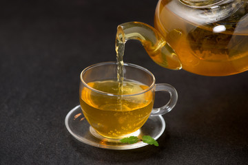 Pouring tea. Cup of hot tea and tea leaf on black stone background.