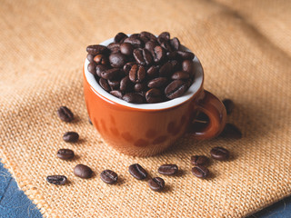 Coffee beans in italian espresso cup on burlap and dark blue black background