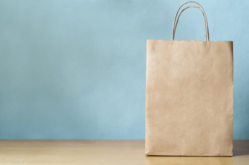 Blank Brown Carrier Bag with Handles on Light Wood Veneer Table with Blue Background