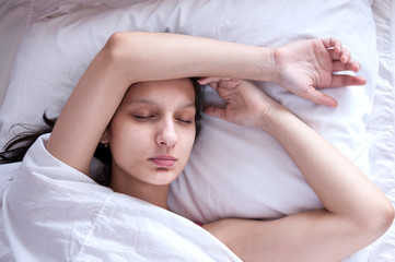 Girl brunette sleeping in her bed on white pillow
