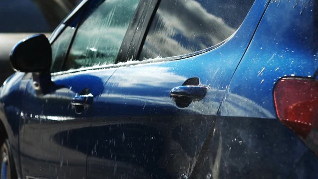 Blue car washed by hand using a water jet wash in a shiny day