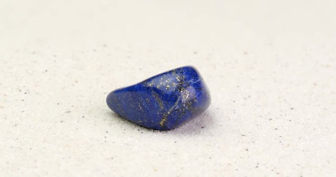 Lapis Lazuli gem rotating on white sand surface. Semi precious gemstone from Afghanistan. Clip contains seamless loop.
