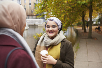 British Muslim Female Friends Talking By River In City