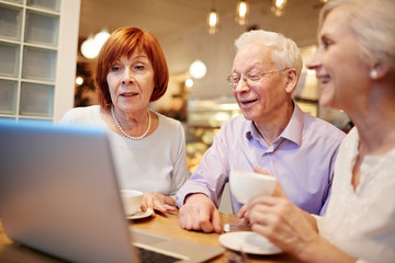 Group of three senior friends sitting in cafe in front of laptop