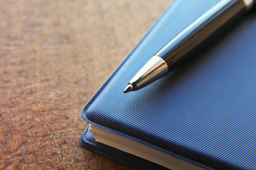 blue notebook and ball pen on an old  wooden background, close up view with copy space.