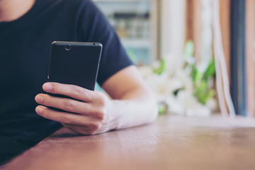 A man holing and using on black smart phone in modern cafe