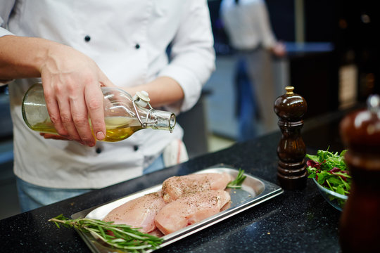 Chef pouring olive oil on raw chicken steak