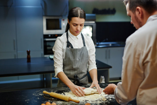 Young apprentice of baker kneading dough for bread
