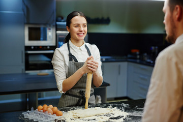 Happy woman with rolling-pin talking to chef while preparing dough