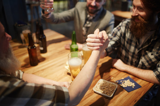 Young and senior men having wrestling competition on pub table - Powered by Adobe