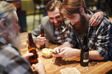 Three bearded men with bottles of beer spending time in pub