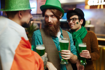 Young friendly men with glasses of beer spending time in pub