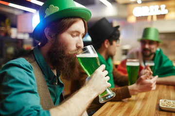 Young bearded man drinking green beer in pub