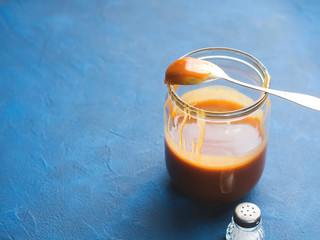 Home made salted caramel in glass jar on dark blue background. Copy space