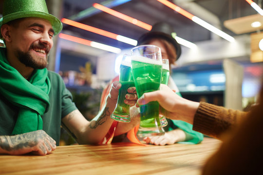 Happy buddies toasting with green beer over table