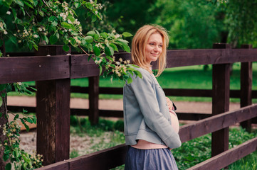 happy pregnant blonde beautiful woman walking outddor in spring park or garden, posing near blooming bush