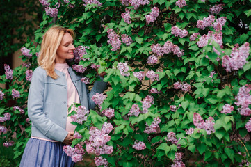 happy pregnant blonde beautiful woman walking outddor in spring park or garden, posing near blooming bush