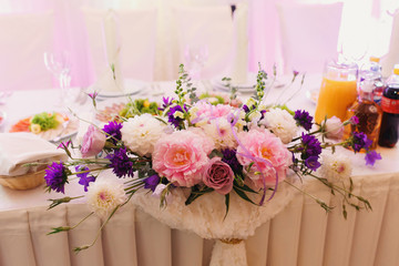 Bouquet of violet pinks and pink roses lies on white dinner table