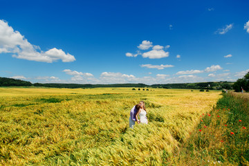 Fototapeta na wymiar Look from afar at groom kissing bride's shoulder while wind blows wheat on field