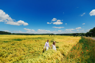 Fototapeta na wymiar Bride and groom walk across field of wheat under deep blue sky