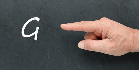Lettre G à la craie sur un tableau noir et montrer du doigt