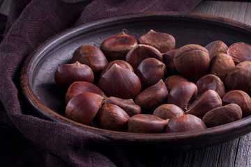 fresh raw chestnuts in a clay bowl, dark photo, selective focus
