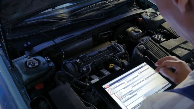 Mechanic in a auto repair shop checking engine using a digital tablet