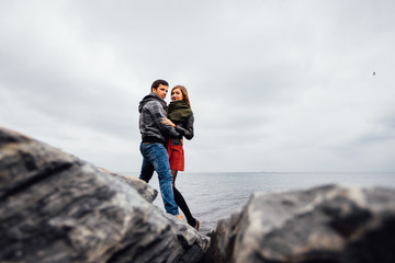 Guy and a girl, the couple posing in a picturesque place rocks, sea, autumn sky.