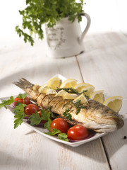 healthy food: two fried sea bass fish served with tomatoes and vegetables on big wooden board over table