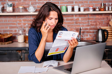 Young woman sitting in the kitchen holding utility bills