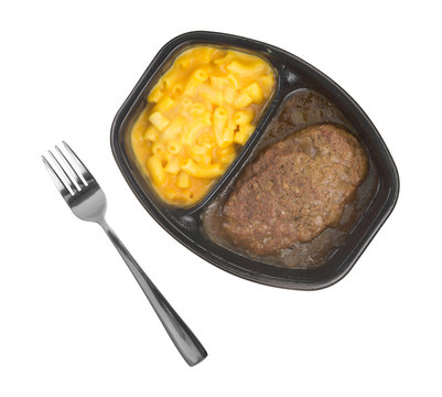 Top view of a Salisbury steak meal with macaroni and cheese TV dinner isolated on a white background with a fork to the side.