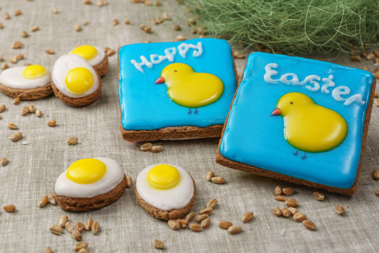 Square cakes with a picture of chickens on a blue background and the words Happy Easter are near gingerbread patterned eggs