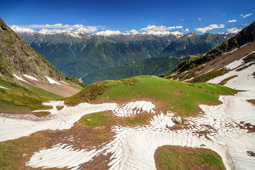 Beautiful scenic landscape of mountain cirque and peaks with snow caps in Caucasus mountains at late spring on sunny day with clear blue sky and fresh greenery forest