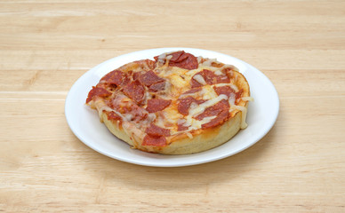 Uncut personal size pepperoni pizza on a white plate atop a wood table. 