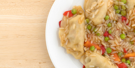 Top close view of a vegetarian potstickers meal on a white plate atop a wood table.