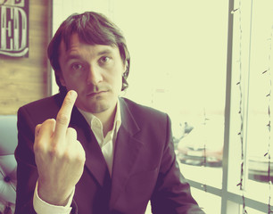 Businessman in cafe shows hand fuck sign