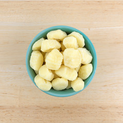 Top view of plain potato gnocchi in a green bowl atop a wood table.