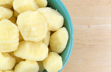 Top close view of plain potato gnocchi in a green bowl atop a wood table.