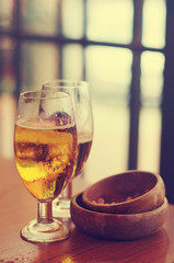 Two glasses of beer and wooden cups for nuts on a table