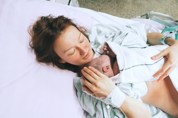 Mother holding her newborn baby after labor in a hospital. - obrazy, fototapety, plakaty