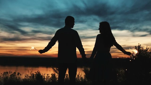 A silhouetted couple takes and evening walk, A silhouetted couple watching on a sunset, Silhouette of a couple at sunset, Loving Couple at Sunset, hand-held sparklers