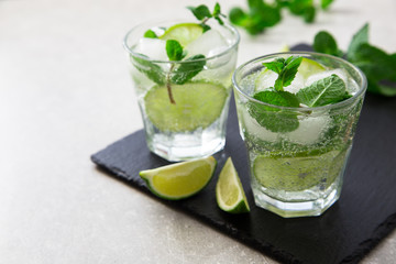 Cold refreshing summer lemonade mojito in a glass on a slate board and stone background.
