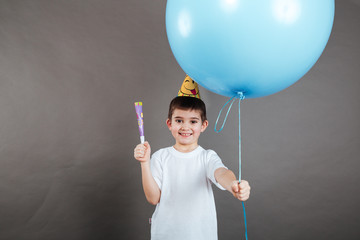 Happy little boy in birthday hat giving you blue balloon
