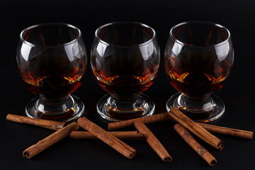 Glasses of cognac and cinnamon sticks on a black background