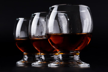 Three glasses with cognac in a row on a black background