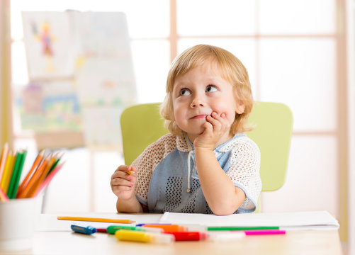 Smiling kid drawing with color pencils in day care center