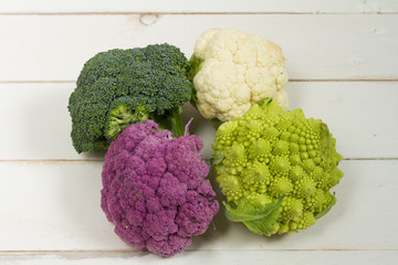 Fresh organic white and purple cauliflower, broccoli, romanesco. On wooden board, bowl, wooden cutting board.